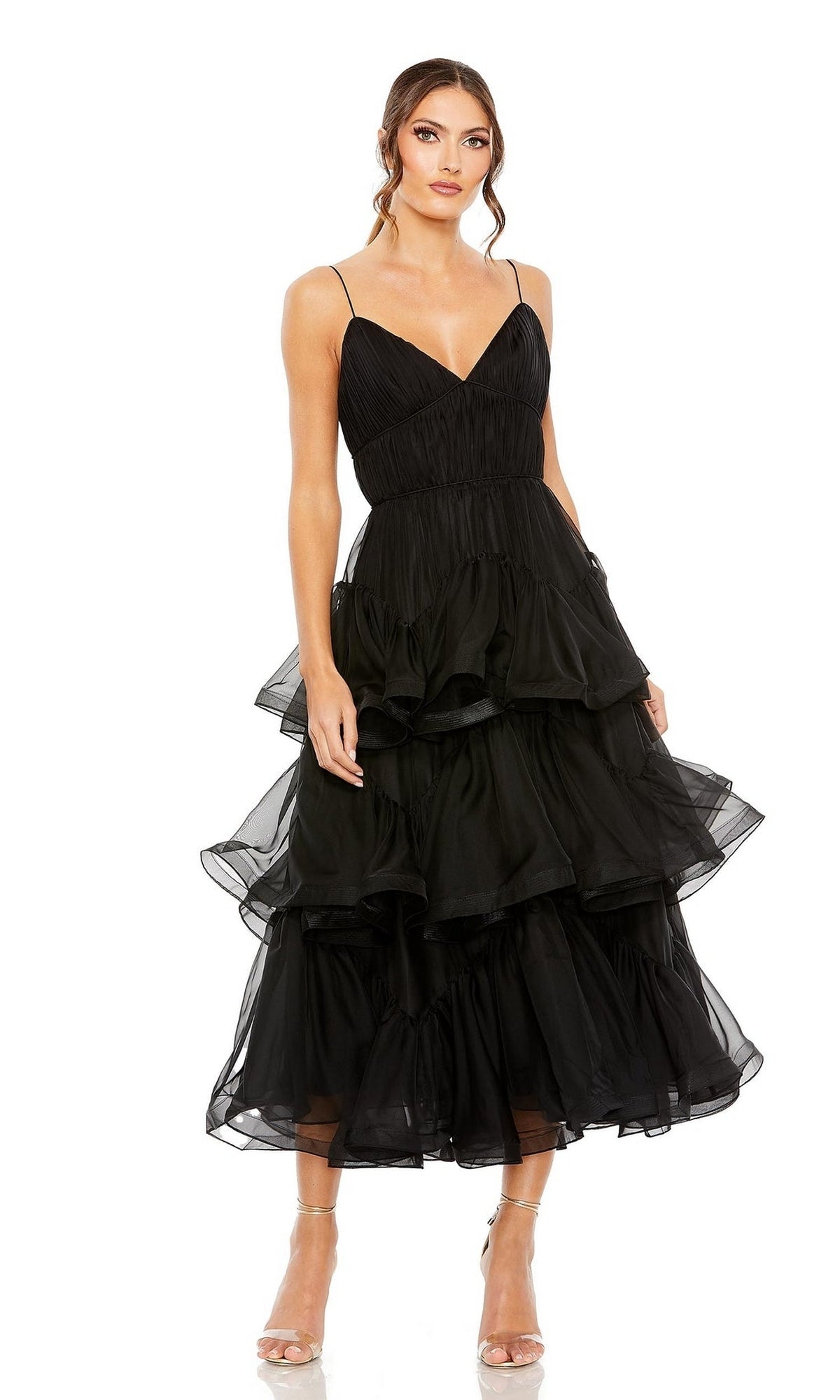 A woman stands against a plain white background wearing the Mac Duggal 68411 midi black wedding guest dress with thin straps and nude high-heeled sandals.